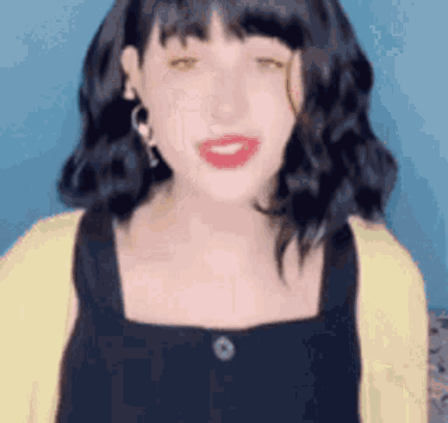 a woman with black hair and red lipstick is wearing a yellow sweater and a black dress .