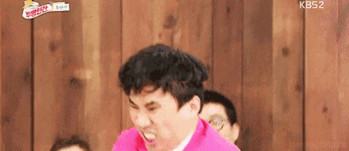 a man in a pink shirt is making a funny face in front of a group of people .