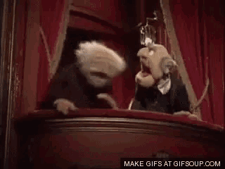 two muppets are standing on a balcony in front of a red curtain .
