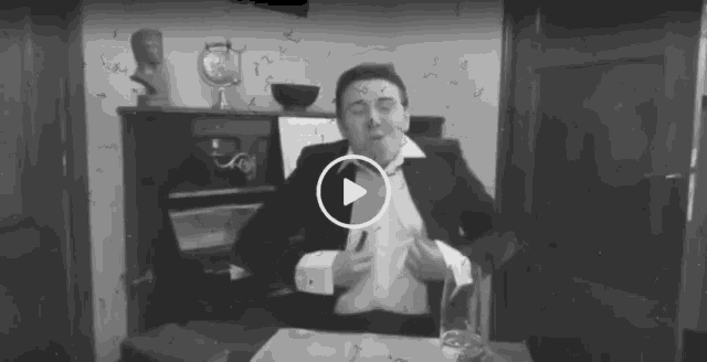 a man in a suit is sitting at a desk with a play button on the bottom right