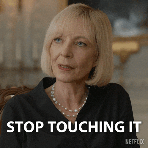 a woman with blonde hair and a pearl necklace is sitting in front of a sign that says stop touching it