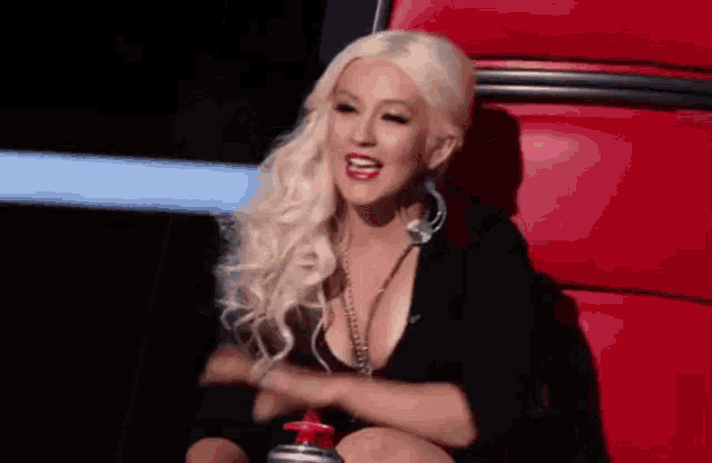 a woman with blonde hair is sitting on a red chair and laughing .