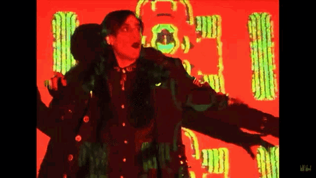 a man in a black coat is standing in front of a red background with the letter i visible