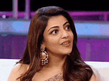 a woman wearing earrings is sitting on a couch and looking at the camera .