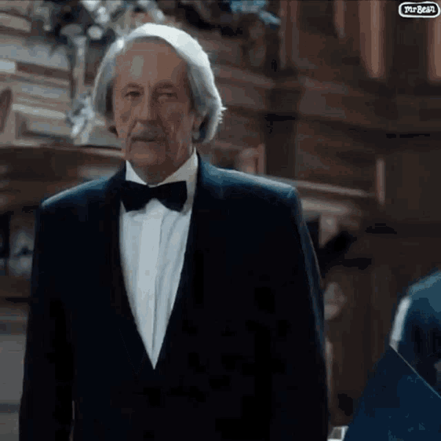 an older man in a tuxedo and bow tie is standing in a room with a sign that says mr. bear