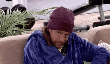 a man is sitting on a couch wearing a purple beanie and a blue robe .