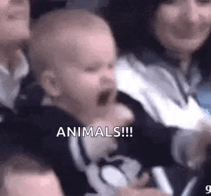 a baby is crying in a crowd of people while a woman holds him .