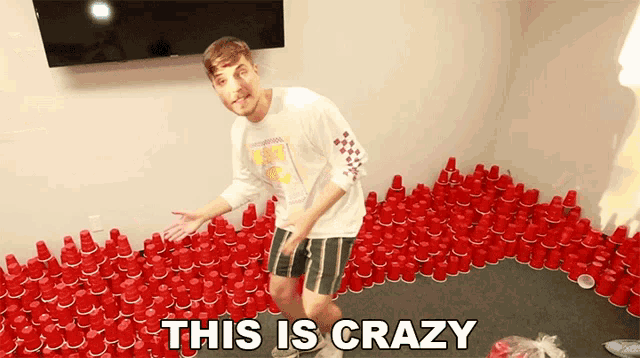a man is standing in a room filled with red cups and the words " this is crazy " next to him