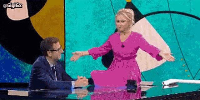 a man and a woman are sitting at a table . the woman is wearing a pink dress .