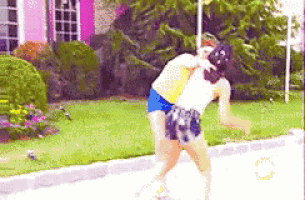 two women are fighting on a sidewalk in front of a house