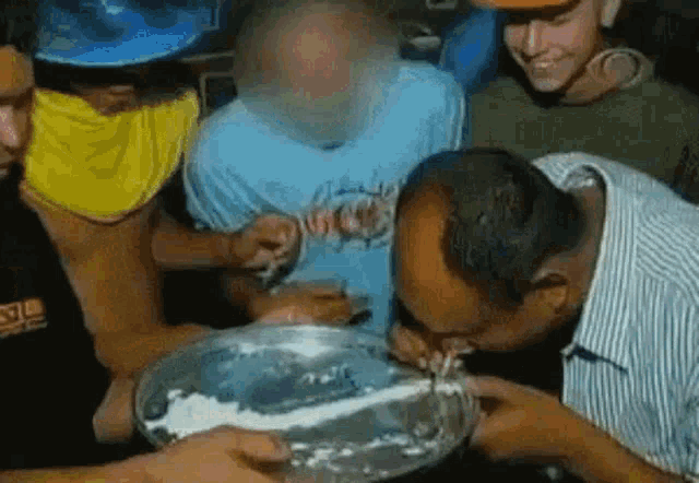 a group of men are eating a cake together and one of them is licking it .