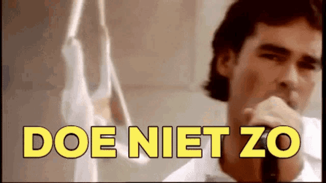 a man is singing into a microphone with the words doe niet zo written above him