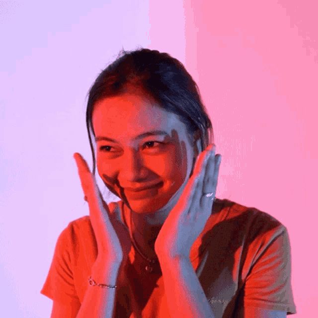 a woman covering her face with her hands with a pink background