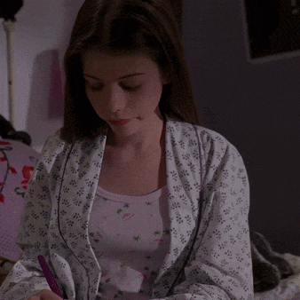 a girl in a pink and white floral pajama top is writing on a piece of paper