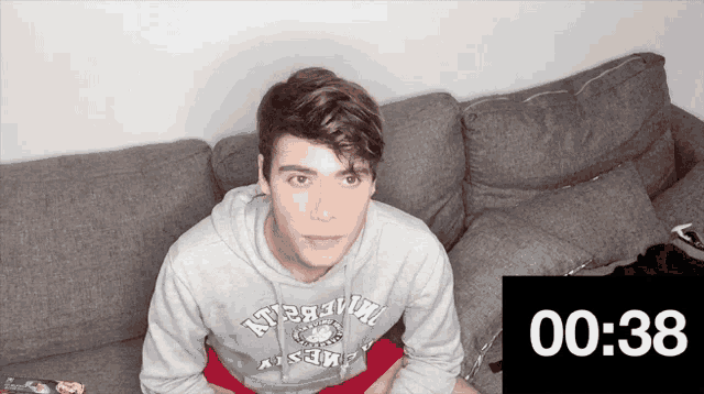 a young man is sitting on a couch wearing a grey sweatshirt that says ' n't ' on the front