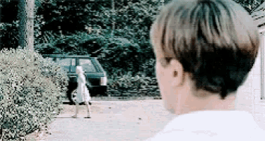 a man in a white shirt is looking at a girl walking down a driveway .