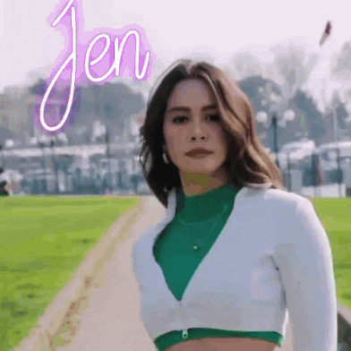 a woman wearing a green crop top and a white cardigan is standing on a sidewalk .