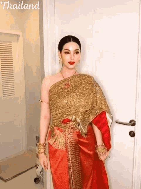 a woman in a red and gold dress from thailand is standing in front of a white door