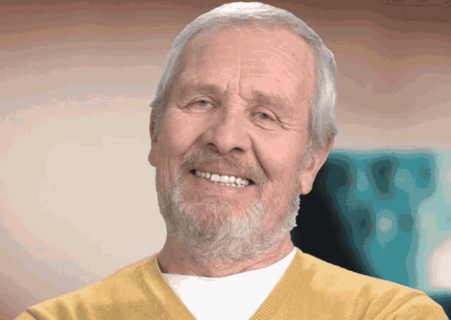 an elderly man with a beard and yellow sweater smiles