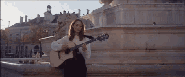 a woman is playing a guitar in front of a fountain in a city .