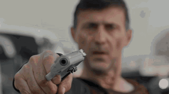 a man pointing a gun at the camera with a blurry background