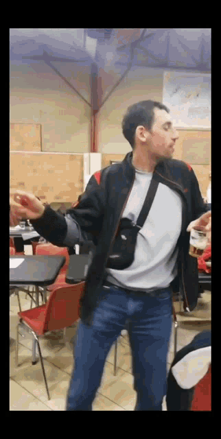 a man in a black jacket is standing in a room with tables and chairs
