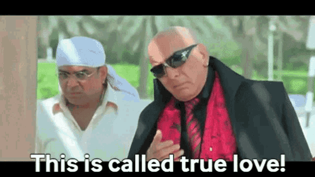 two bald men are standing next to each other and one of them is wearing sunglasses and a red shirt .