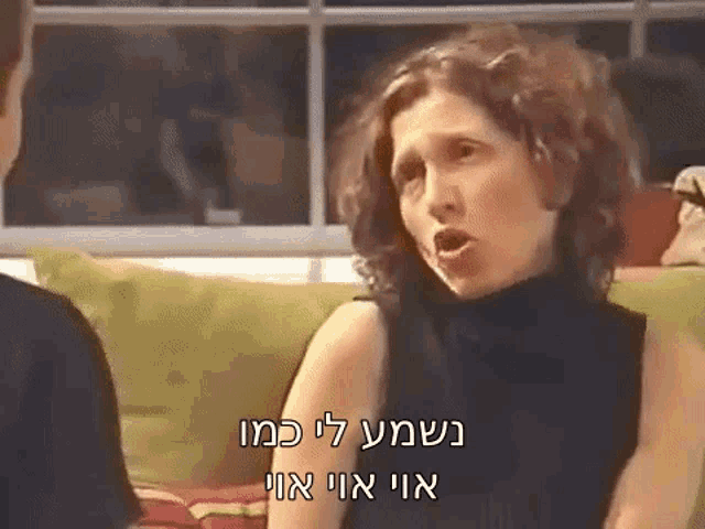 a woman is sitting on a couch talking to a man in a video in hebrew .