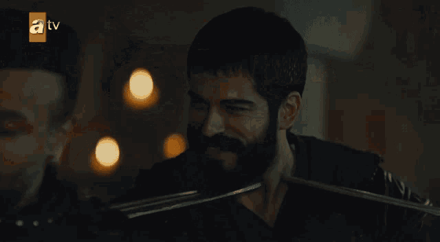 a man with a beard is in a dark room with a tv logo in the background