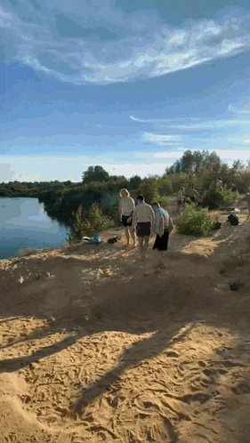 a group of people are walking on a sandy beach near a lake