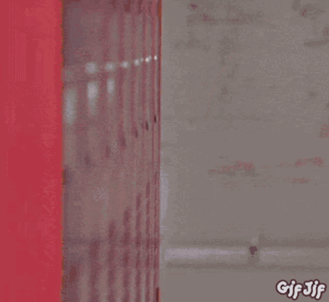 a man in a suit and tie is peeking out from behind a red locker with gif 3jf written on the bottom
