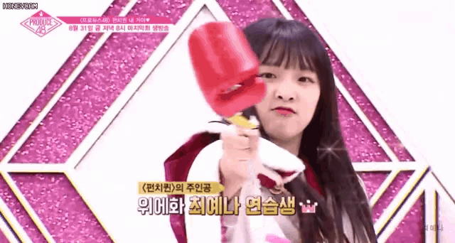 a girl is holding a red object in front of a pink background that says ' produce 48 ' on it