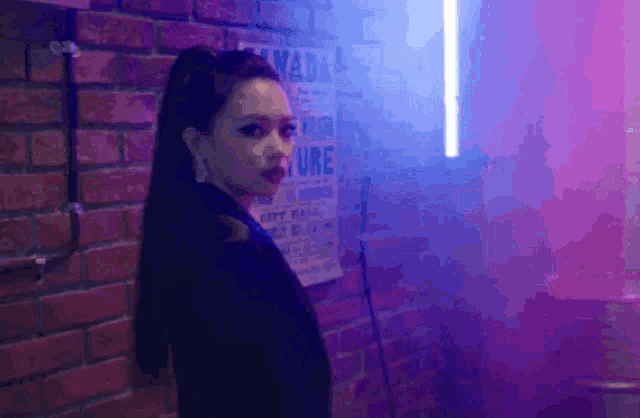a woman is standing in front of a brick wall in a dark room with purple lights .