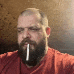 a bald man with a beard is smoking a cigarette .