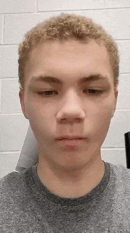 a close up of a young man 's face with a gray shirt on .
