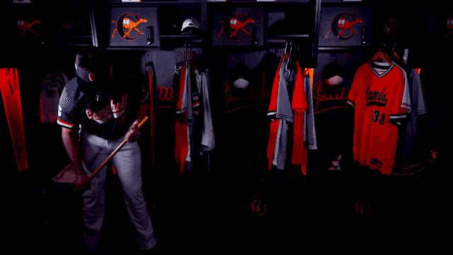 a man in a campbell jersey holds a bat in a locker room