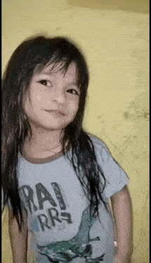 a little girl with long hair is wearing a shirt with a dinosaur on it and looking at the camera .