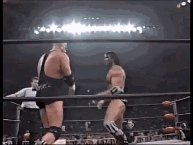 two men are wrestling in a ring with a referee .