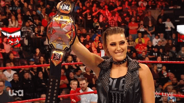 a woman in a wrestling ring holds up a wwe championship belt in front of a crowd