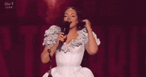 a woman in a white dress is speaking into a microphone on a stage .