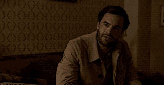 a man in a trench coat sits on a couch