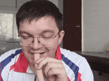 a man wearing glasses and a red white and blue jacket bites into a sausage