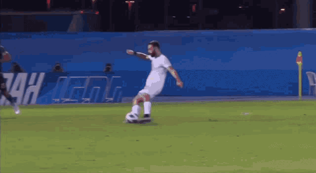 a man kicking a soccer ball on a field with a sign behind him that says tah