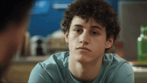 a young man with curly hair looks at the camera