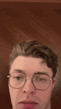 a close up of a man wearing glasses against a wooden background