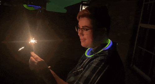 a person wearing glow in the dark necklaces is holding a sparkler in their hand