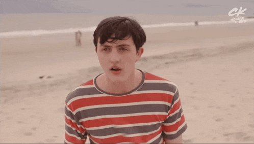 a man in a striped shirt is standing on the beach with a red ball in front of his face