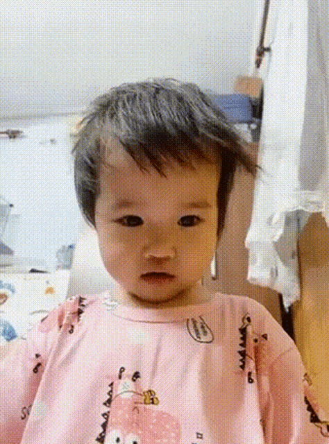 a baby in a pink shirt with a bear on it looks at the camera