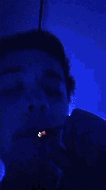 a person is smoking a cigarette in a dark room with blue lights .