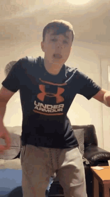 a young man is wearing a black under armour shirt and dancing in a living room .